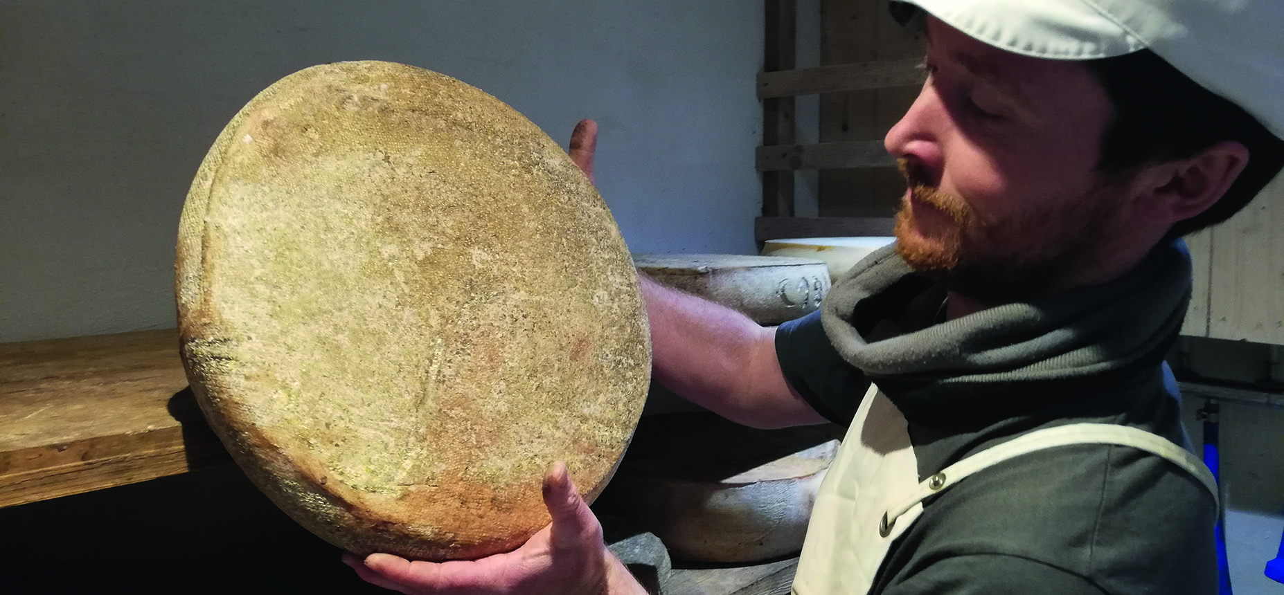 Mathis Baumann tenant une meule de fromage dans sa fromagerie